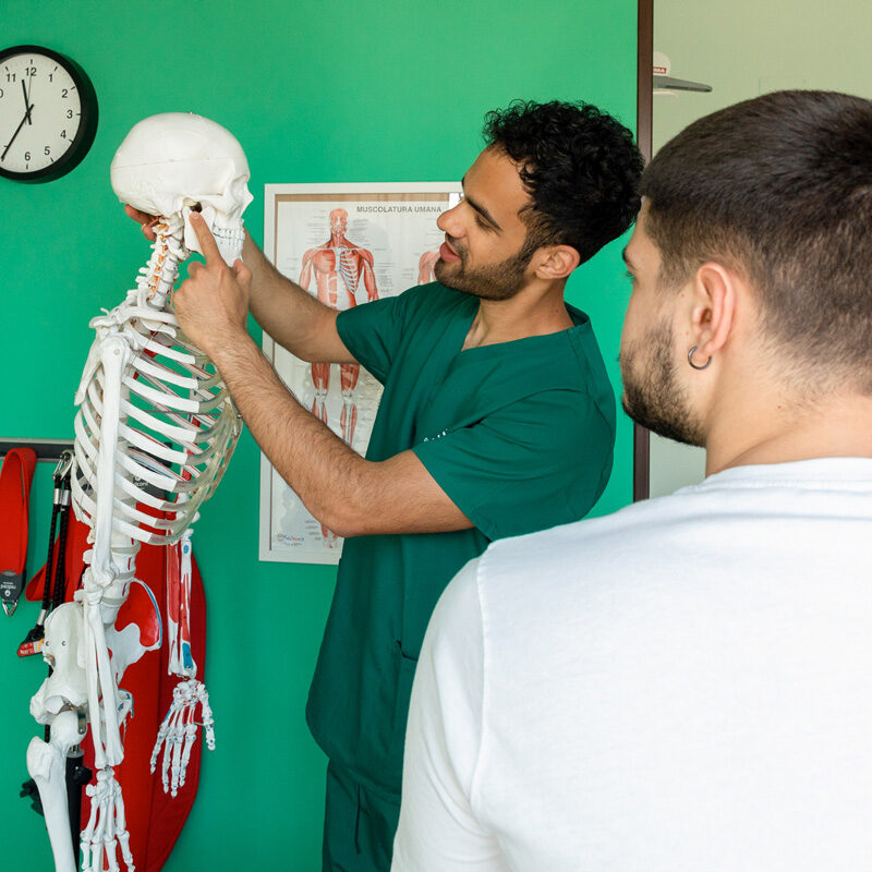 Dottore osteopata e fisioterapista Dario De Martino indica al paziente uomo il punto in cui sente dolore utilizzando il modellino di uno scheletro.